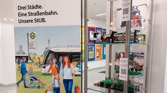 Modell der 6. Lego-Planungswerkstatt in einer Glasvitrine, daneben ein Roll Up zur Stadt-Umland-Bahn.