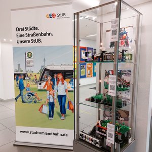 Modell der 6. Lego-Planungswerkstatt in einer Glasvitrine, daneben ein Roll Up zur Stadt-Umland-Bahn.